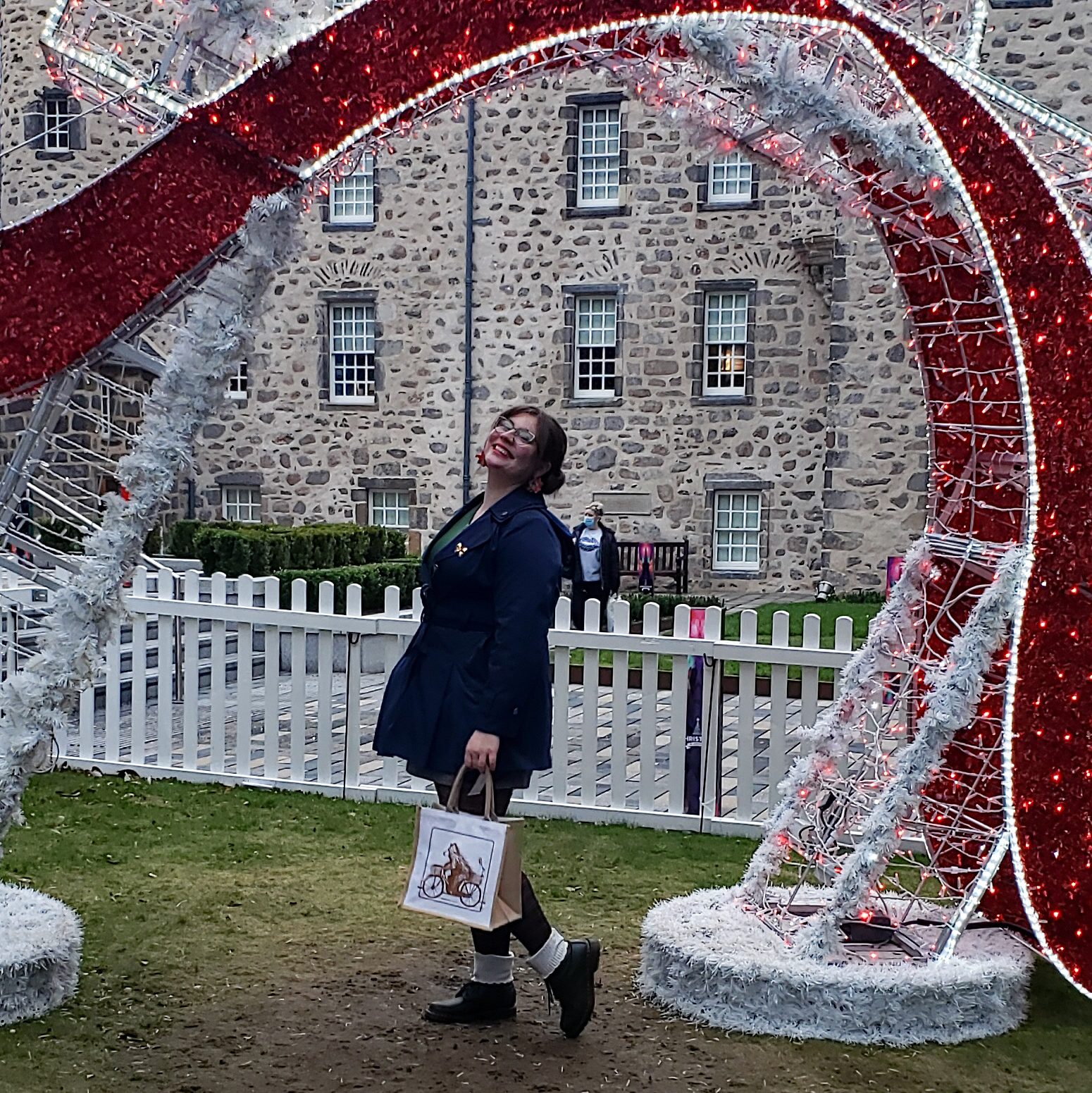 Michelle posing at the Aberdeen Christmas Village Smiling and holding a bag with a drawing of a bear riding a bicycle. 